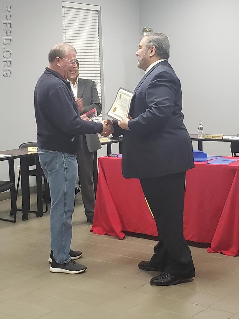 Trustee Brian A. Bernardoni congratulates Trustee Patrick Lorenz with a service award and challenge coin from the Illinois State Fire Marshal.  