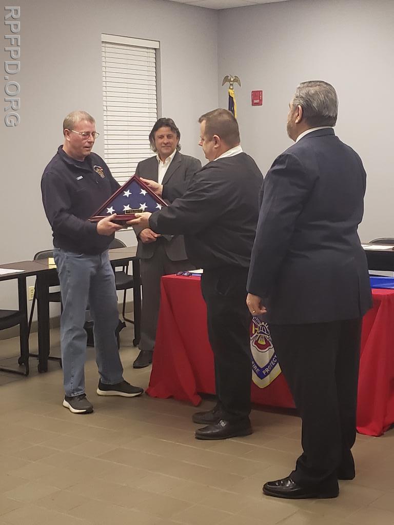 Fire Chief Ketchen presents Trustee Patrick Lorenz with a ceremonial flag during his last meeting with the Board of Trustees. Trustee Lorenz has served on the Board for 16 years.  
